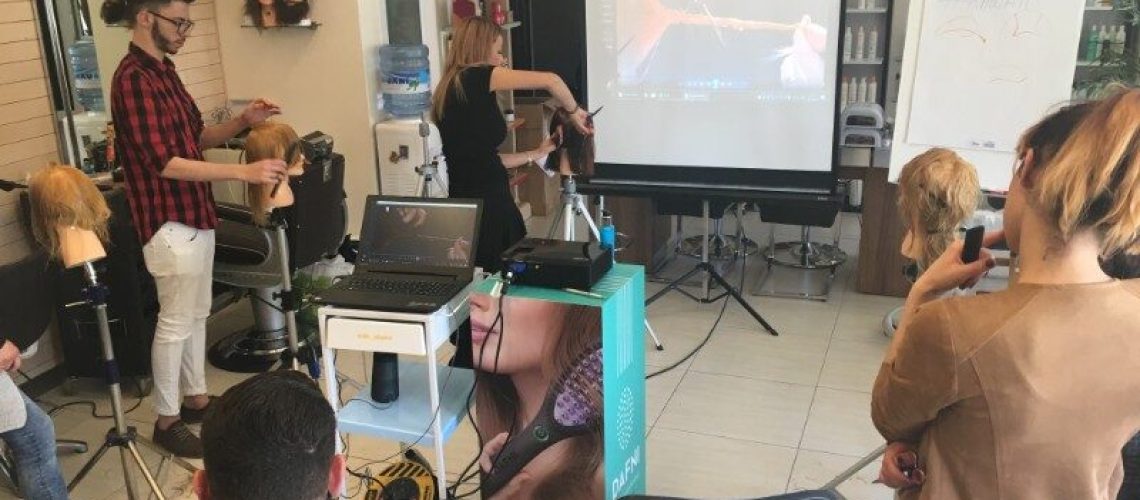 Stylist demonstrating on a mannequin head beside a projection screen