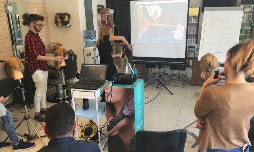 Stylist demonstrating on a mannequin head beside a projection screen